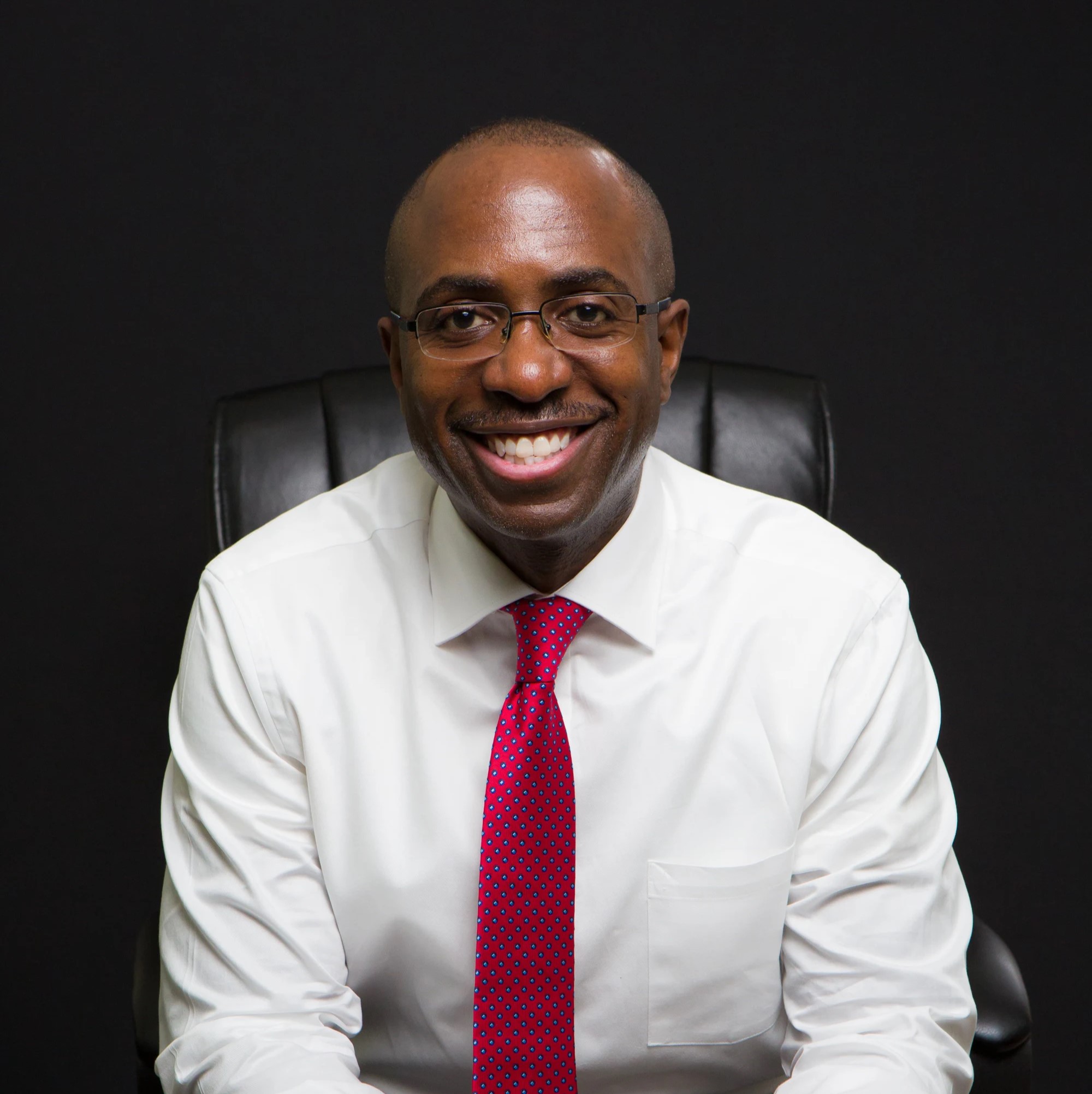 Man in white suit smiling in front of the camera in black background